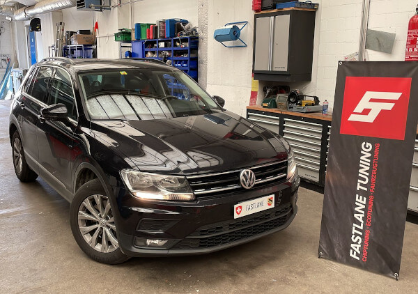 Ein schwarzer VW Tiguan 2.0 TDI steht neben dem Banner von Fastlane Tuning Schweiz