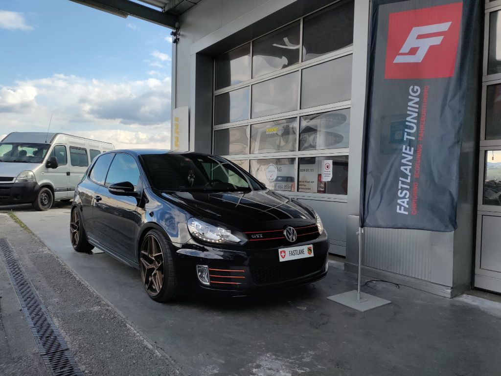 Ein schwarzer Volkswagen Golf Mk6 GTI parkt vor der Garage neben der Fastlane Tuning Schweiz-Flagge