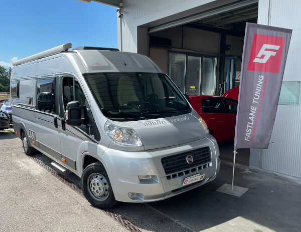 Ein graues Fiat Ducato Malibu Wohnmobil steht neben der Fastlane Tuning Schweiz Flagge.