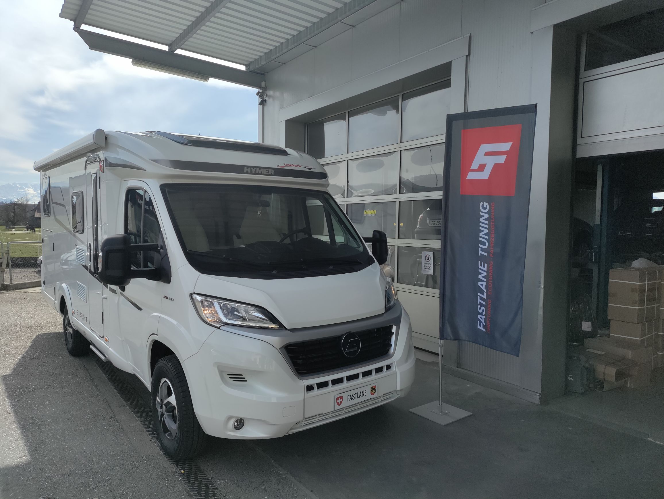 Ein weisser Fiat Ducato III 2.3 Multijet steht vor der Garage neben der Fastlane Tuning Schweiz Flagge