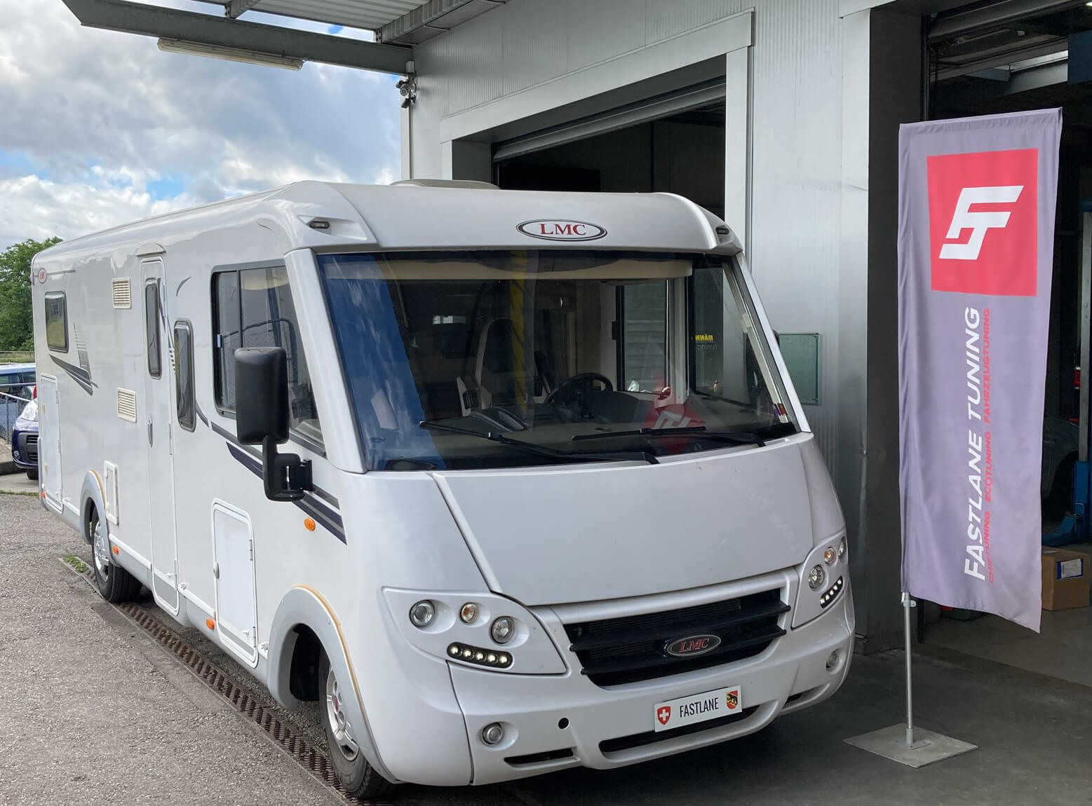 Ein weiss LMC 730G Wohnmobil steht beim der Fastlane Tuning Schweiz Flagge