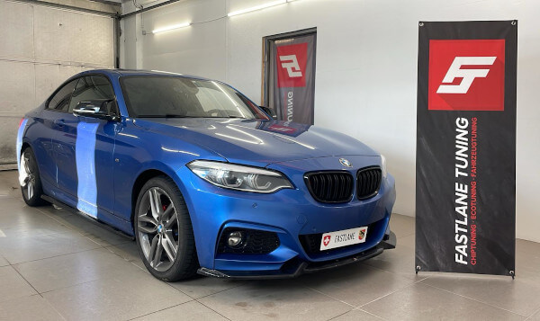 Ein blaues BMW 218d 2-Türer Coupé steht neben dem Banner der Fastlane Tuning Schweiz GmbH