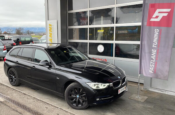 Ein schwarzer BMW 335d Kombi (Touring) steht neben der Fastlane Tuning Schweiz Flagge