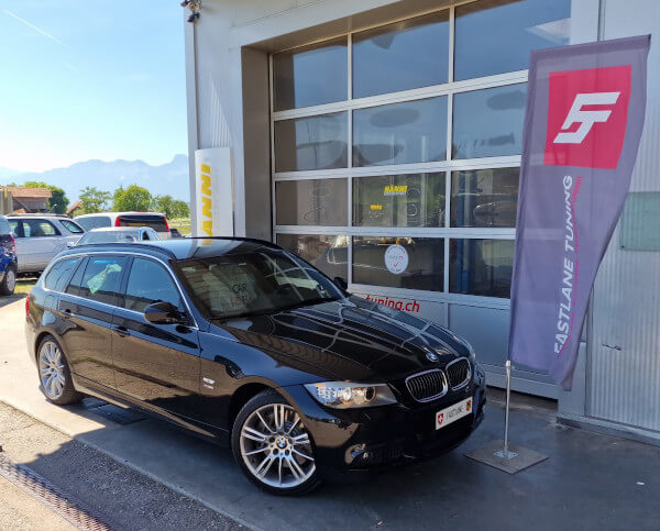 Ein schwarzer BMW 335i E91 Kombi steht neben der Fastlane Tuning Schweiz Flagge.