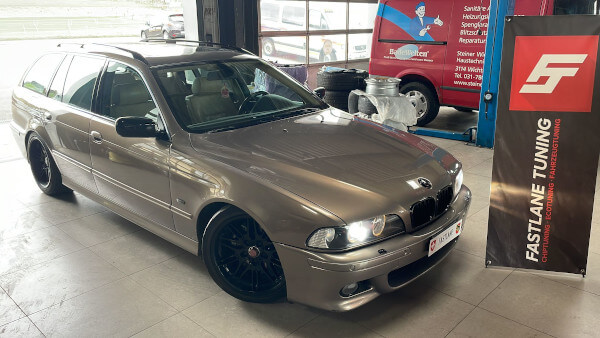 Ein hellbrauner BMW 525d Kombi steht neben dem Banner der Fastlane Tuning Schweiz GmbH