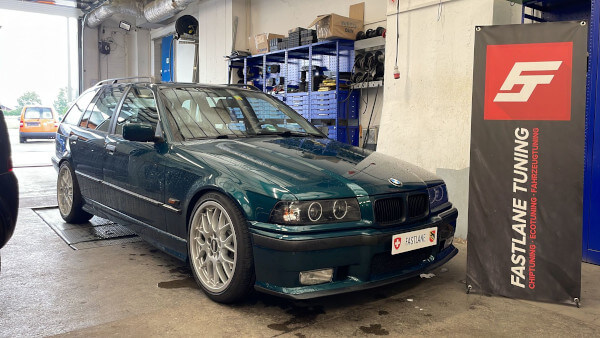 Ein smaragdgrüner BMW 320i E36 steht neben dem Banner der Fastlane Tuning Schweiz GmbH