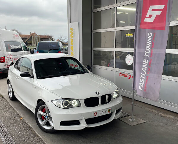 Ein weiss BMW M135i N54 steht neben das Fastlane Tuning Schweiz flagge