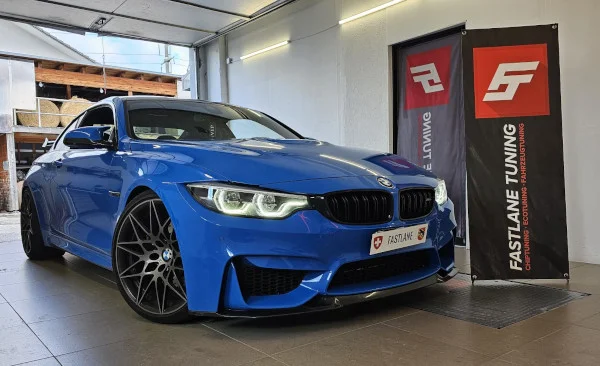 Ein leuchtend blaues BMW M4 Competition Coupé steht neben dem Banner der Fastlane Tuning Schweiz GmbH