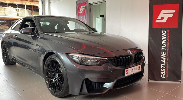 Ein kohlegrauer BMW M4 Competition steht neben dem Banner der Fastlane Tuning Schweiz GmbH