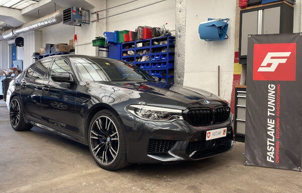 Ein schwarzer BMW M5 F90 mit Motor- und Getriebetuning steht neben dem Banner der Fastlane Tuning Schweiz GmbH.