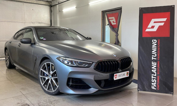 Ein mattgrauer BMW M850i GranCoupe steht neben dem Banner der Fastlane Tuning Schweiz GmbH