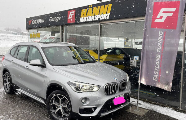 Ein silberner BMW X1 20d xDrive steht vor dem Showroom von Fastlane Tuning Schweiz im Schnee.