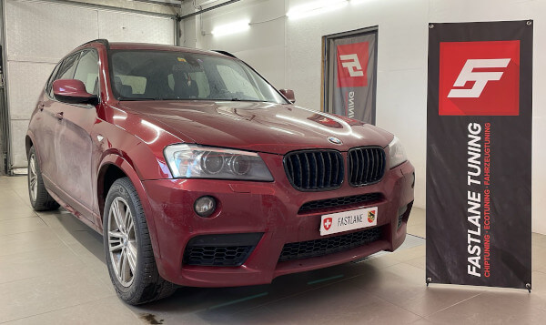 Ein maronfarbener BMW X3 35i steht neben dem Banner der Fastlane Tuning Schweiz GmbH