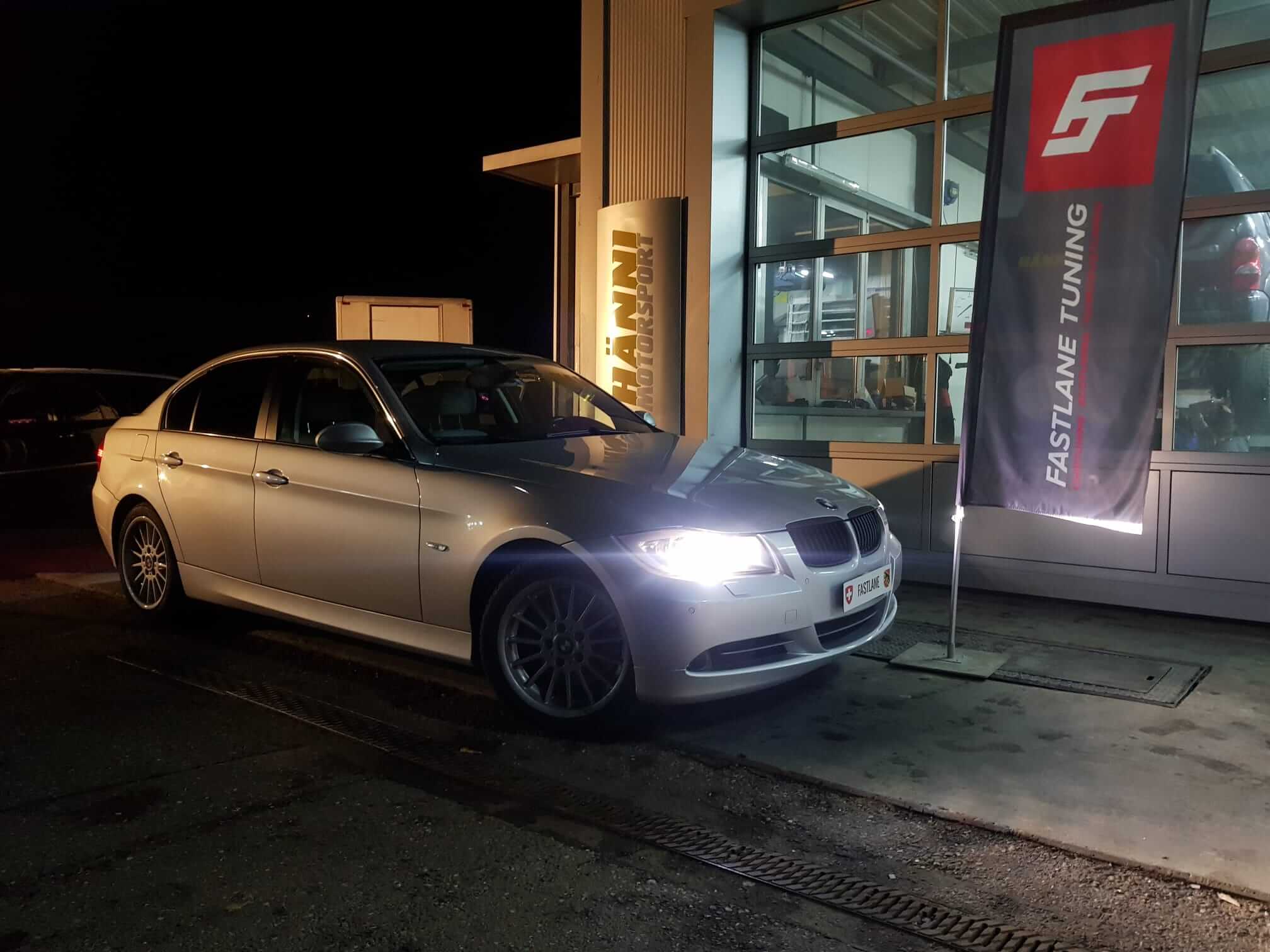 Ein grauer BMW 330i E9X steht neben der Fastlane Tuning Schweiz Flagge