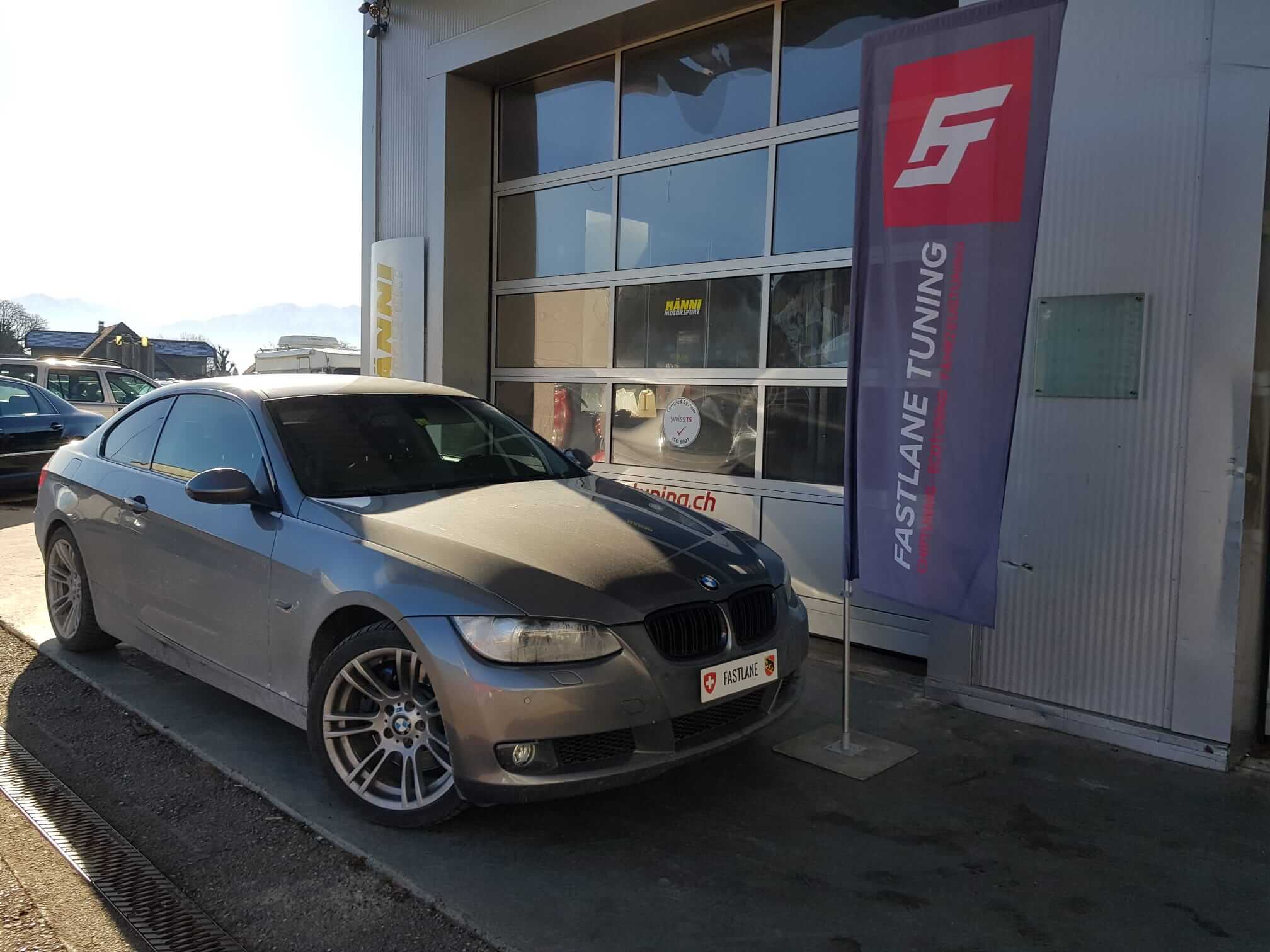 Ein grau BMW 335i N54 steht neben den Fastlane Tuning Schweiz flagge