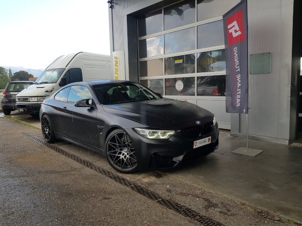 Ein mattschwarzer BMW M4 der Rennserie steht neben der fastlane tuning schweiz Flagge