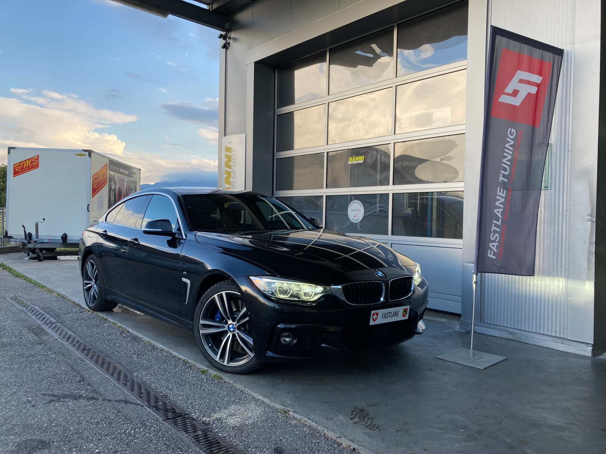 Ein schwarzer BMW M440i steht vor der Garage neben der Fastlane Tuning Schweiz Flagge.