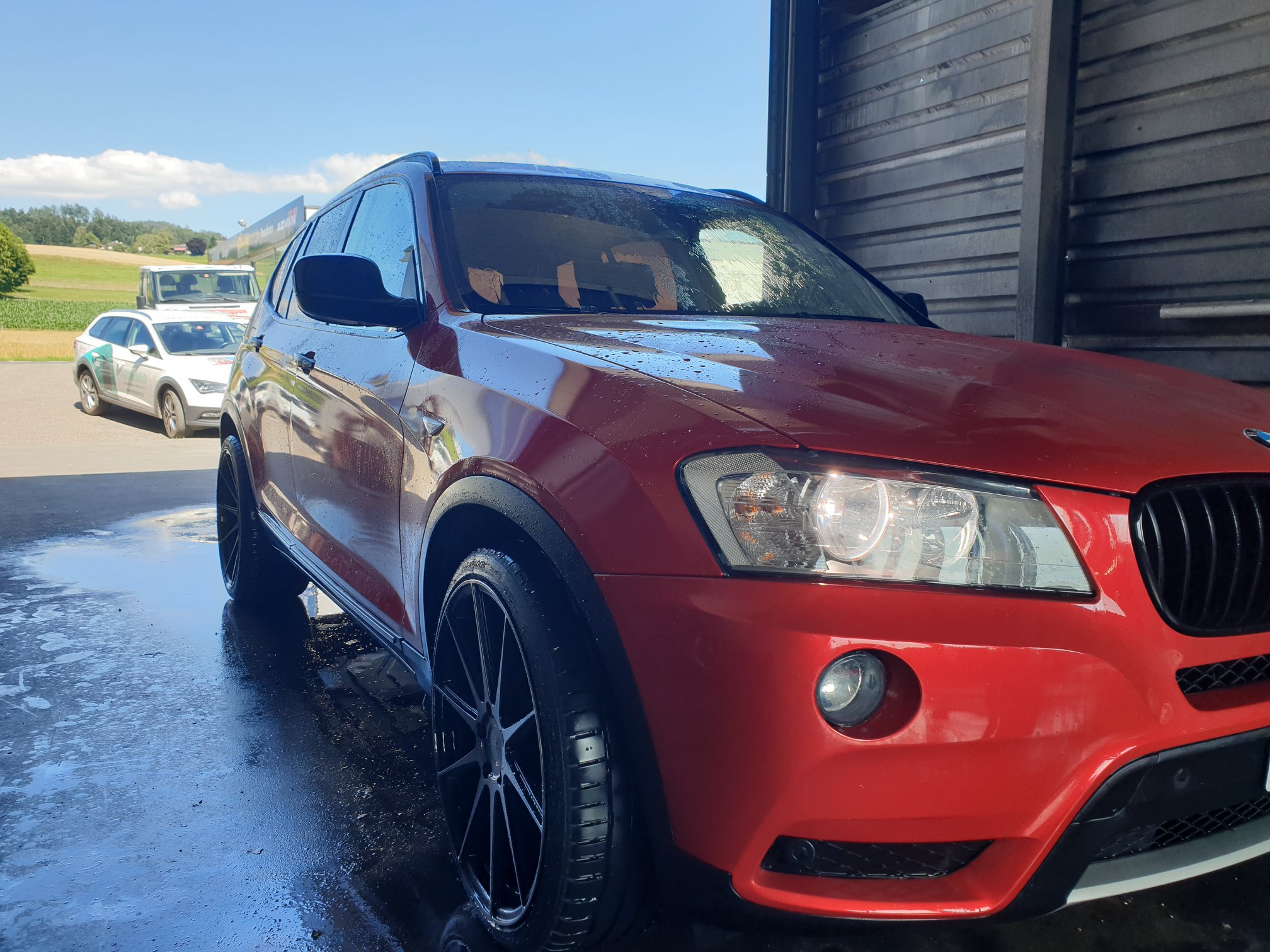 Ein leuchtend roter und orangefarbener BMW E Series X3 2.0 Diesel steht in der Waschanlage der Hanni Motorsport Garage.