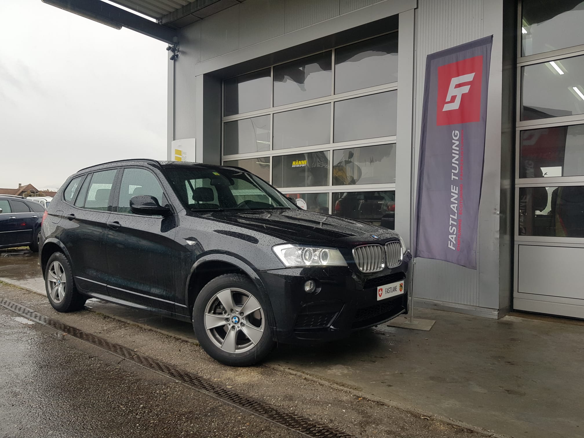 Ein schwarz BMW X3 steht neben den Fastlane Tuning Schweiz flagge